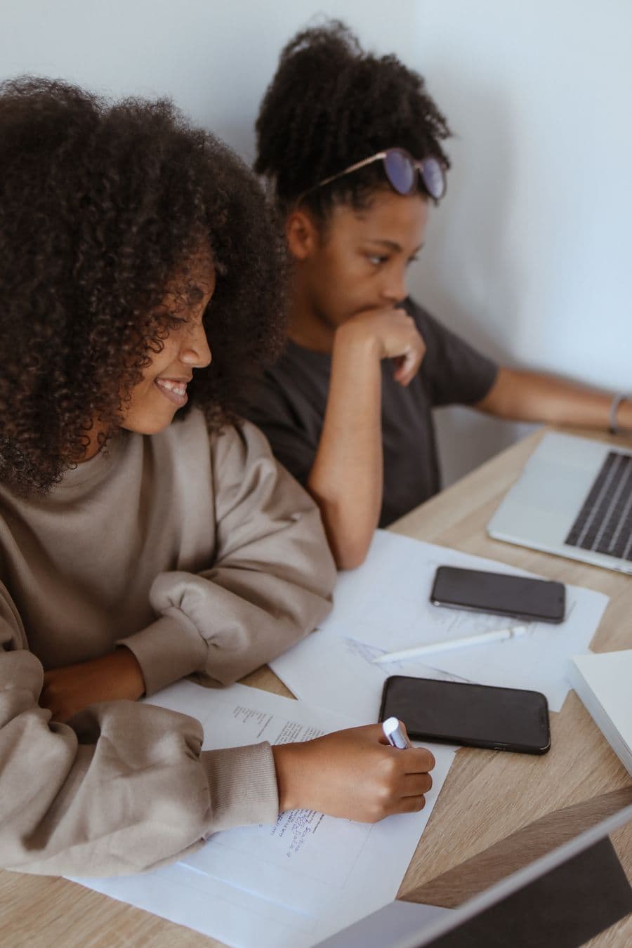Two women reviewing paperwork together beside their laptops